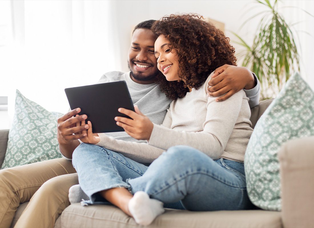 About Our Agency - Happy Young Couple Using a Tablet at Home on the Couch