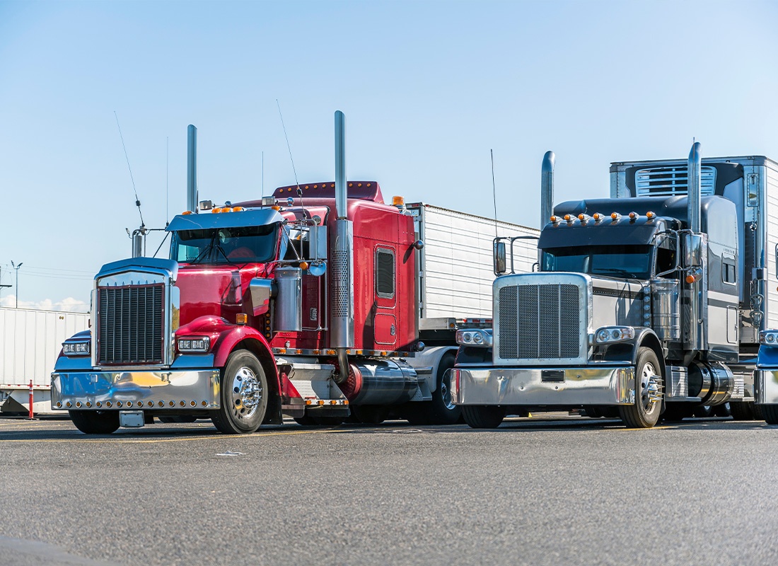Business Insurance - Big Rigs Semi Trucks With Reefer Semi Trailers Standing in a Row on Truck Stop Parking Lot Waiting for Delivery Schedule