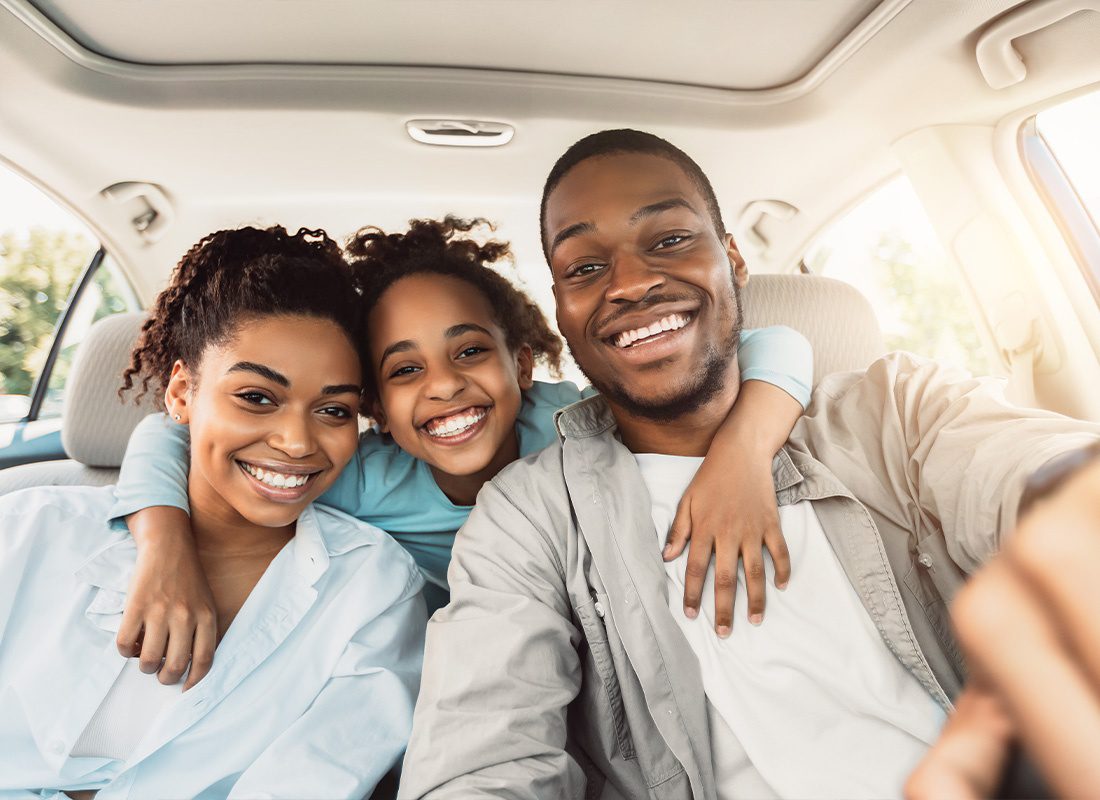 Insurance Solutions - Joyful Young Family Hugging and Sitting in a Car During a Road Trip